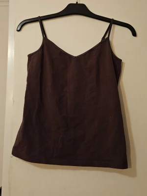 Mörkbrun linnetopp med smala band - En enkel och stilren mörkbrun linnetopp med smala axelband och v-ringad hals. Materialet känns mjukt och lätt, bomull.