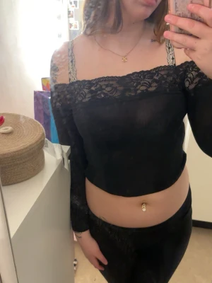 Svart offshoulder croppad spets-topp - Svart offshoulder topp med croppad passform och spetsdetaljer längs överkanten. Tunn och lätt genomskinlig, sitter tight och framhäver axlarna.