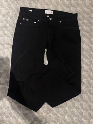 Svarta jeans från Calvin Klein - Snygga svarta jeans från Calvin Klein Jeans med raka ben och klassisk femficksdesign. Jeansen har silverfärgade detaljer och diskret CK-logo på myntfickan. Tillverkade i ett mjukt och stretchigt denimtyg som sitter skönt hela dagen. Köpta för 1000 och använda 3 gånger. Tvek inte att skriva vid frågor eller funderingar!