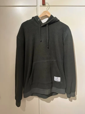 Mörkgrå fleece hoodie från Björn Borg - Mysig mörkgrå hoodie från Björn Borg i fleece med huva och dragsko. Stor känguruficka framtill och ribbade muddar vid ärmar och nederkant. Perfekt för chill dagar eller när du vill hålla dig varm.