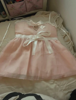 Söt rosa axelbandslös kortklänning - Supersöt rosa topp med vita band och rosett i midjan, spetsdetaljer vid urringningen och ett hjärta av pärlor framtill. Toppen är ärmlös och har en romantisk, luftig känsla som passar perfekt till sommaren. Finns band så man kan knyta toppen runt halsen! Eller ha som tubtopp :)