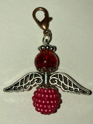 Röd ängelberlock med pärlor - Handgjord lycko ängel av mig med silverfärgade vingar, röd glaspärla som huvud och en klarröd pärlformad kropp. Fästes enkelt med karbinhake. Perfekt som smyckesdetalj eller väsksmycke. Frakt 22-100kr. Kontakta mig om du har frågor eller vill köpa