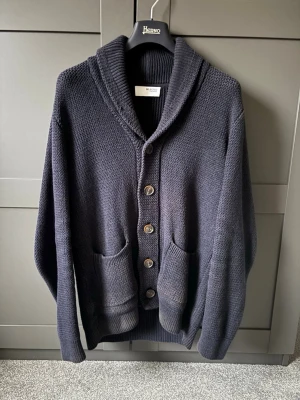 Mörkblå stickad kofta Selected Homme - Mysig mörkblå stickad kofta från Selected Homme med grov struktur, sjalkrage och fyra stora knappar framtill. Två rymliga fickor framtill och ribbade muddar. Perfekt för lager på lager! Nypris:679kr 