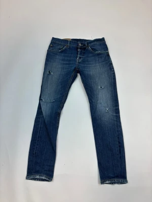 Dondup - Säljer ett par blå jeans med slitningar och raka ben. Jeansen har klassisk femficksdesign, knappgylf och snygga slitdetaljer på både fram- och baksida. Perfekta för en avslappnad och trendig look.
