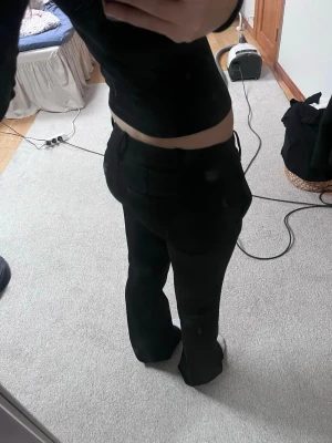 Svarta kostymbyxor med raka ben - Säljer ett par svarta kostymbyxor med klassisk rak passform och låg midja. Byxorna har diskreta bakfickor och är sydda i ett mjukt, välsittande material som ger en clean look. Perfekta till en snygg topp eller skjorta.