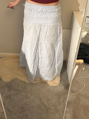 Ljusblå långkjol med smock - Ljusblå långkjol med bred smock i midjan som ger en bekväm och flexibel passform. Kjolen har en luftig och flowy känsla, perfekt för varmare dagar. Tillverkad i ett tunt bomullsliknande material som känns svalt mot huden.