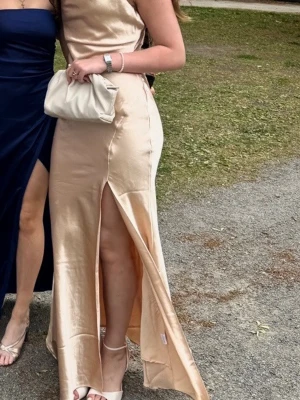 Champagnefärgad långklänning med slits - En champagnefärgad satin balklänning med hög slits framtill och figurnära passform🥰Den är öppen i ryggen och passar med både uppsatt och nedsatt hår🙏🥰Köpt från zalando True decadence för 1400kr och endast använd en gång🩷 på näst sista bilden kan du se hur den gröna varianten sitter på modellen då orginal artikeln på den champagnefärgade klänningen inte längre är tillgänglig🥰🩷 klänningen går såklart att ha till andra tillfällen såsom bröllop eller finare tillfällen🥰skriv om du har några frågor!🙏🩷