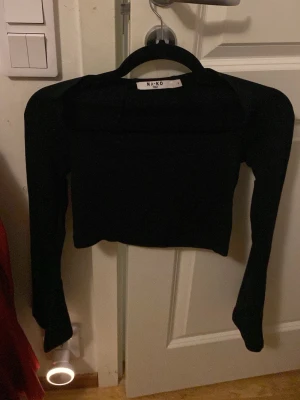 Svart croppad trumpetärmad topp från NA-KD - Säljer en svart croppad topp från NA-KD i storlek S. Toppen har långärmade, utsvängda ärmar och en stilren, enkel design. Materialet är mjukt och stretchigt, perfekt för att skapa en cool look. Passformen är slim och toppen är enfärgad utan mönster.