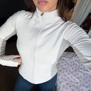 Vit och grå zip-up jacka - Oysho - Snygg vit och ljusgrå träningsjacka med hög krage och hel dragkedja framtill. Jackan har långa ärmar och en sportig, figurnära passform. Fickor på vardera sida🩵sista bilden visar en liten defekt som inte går bort i tvätten!