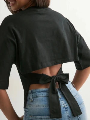 Nelly - Open Back Tie Tee - Svart topp i bomull med korta ärmar och rund hals. Baksidan har en öppen rygg med breda band som knyts i en stor rosett. Säljer då den aldrig kommit till användning. 