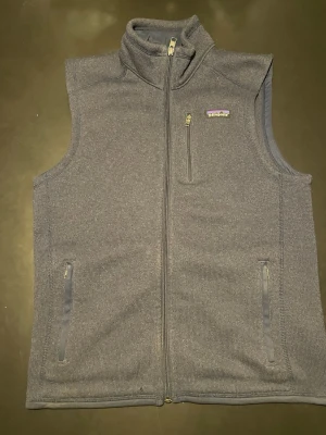 Mörkgrå fleeceväst från Patagonia - Säljer en mörkgrå fleeceväst från Patagonia med hel dragkedja, hög krage och tre fickor med dragkedja. Västen är i mjukt fleecematerial och gör varje outfit något lite exakta. Prekt inför kommande våren. Köpte västen helt ny för 1300kr. Obs västen har ett minimalt hål (se sista bilden) men inget som man tänker på.