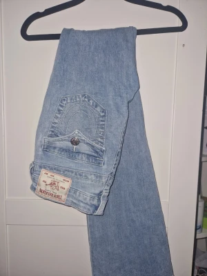 True Religion ljusblå bootcut jeans -  ( pris kan diskuteras) Aldrig använt bara provat! Säljer ett par ljusblå jeans från True Religion med klassisk fickdesign och logopatch bak. Jeansen har bootcut-snitt tillverkade i mjukt jeanstyg. Perfekt för dig som gillar ikoniska detaljer och snygg siluett. Dem var lite för stora så därför säljer jag!