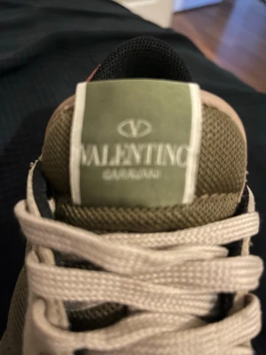 Valentino Garavani sneakers i beige och oliv - Snygga sneakers från Valentino Garavani i beige och olivgrönt med mesh och mockadetaljer. Klassisk snörning och svart yttersula med rutmönster. Perfekta för dig som vill ha en stilren och exklusiv look.