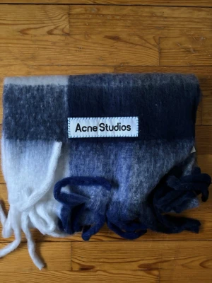 Rutig ullhalsduk från Acne Studios - Mysig halsduk i tjock, fluffig ull från Acne Studios. Färgblock i mörkblått, vitt och grått med stora rutor och långa fransar i ändarna. Perfekt accessoar för att lyfta din outfit med en trendig touch.