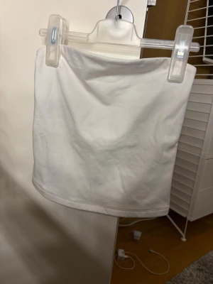 Vit tub topp  - Säljer en enkel och stilren vit bandeau topp/ tubtopp. Toppen är axelbandslös och har en rak, tight passform. Den är endast använd en gång. Super mjukt material.