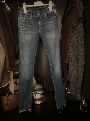 Blå skinny jeans från Replay - Säljer ett par blå skinny jeans från Replay med klassisk femficksmodell och snygga slitningar. Jeansen har låg midja och är tillverkade i stretchig bomullsdenim för skön passform. Perfekta till vardags och enkla att matcha med olika stilar.