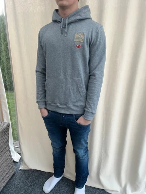 Grå hoodie Morris med brodyr - Riktigt snygg grå hoodie från Morris i storlek XL . Sitter som Strl L, jag själv är 184 cm. Guldbroderat emblem och brittisk flagga på bröstet. Inga skavanker.