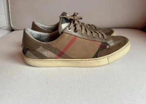 Burberry sneakers - Snygga sneakers från Burberry i klassiskt beige och brunt rutigt mönster med röda detaljer. Skorna har snörning, rund tå och platt sula. Materialmix av canvas och skinn ger en exklusiv känsla och ikonisk look.
