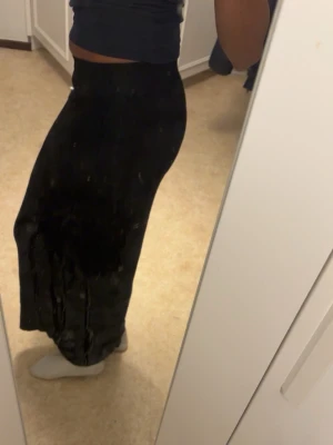 Svart långkjol i mjukt material - Säljer en svart ribbad långkjol med enkel och stilren design. Kjolen har en rak passform och är gjord i ett mjukt, följsamt material som ger en snygg siluett. Kjolen är helt oanvänd med prislapp kvar!