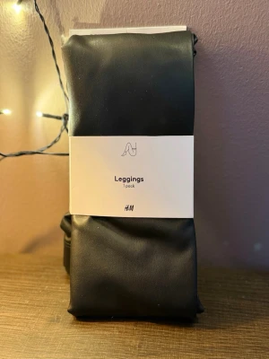 Svarta leggings i skinnimitation H&M - Snygga svarta leggings från H&M i storlek XL. De har en stilren look i skinnimitation som ger en cool vibe till vilken outfit som helst. Perfekta att matcha med oversized tröjor eller crop tops för en trendig stil. Helt nya oöppnade.
