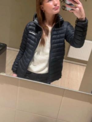 Svart dunjacka från Peak Performance - Säljer en svart dunjacka från Peak Performance med quiltad design och dragkedja framtill. Jackan har en smal passform och hög krage, perfekt för kyliga dagar. Klassisk och stilren modell som funkar till det mesta.