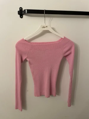 Rosa ribbad topp från BikBok - Supersnygg ljusrosa ribbad topp från BikBok med offshoulder-modell och långa ärmar. Stretchigt material som sitter tight och framhäver figuren. Perfekt att styla med jeans eller kjol för en trendig look.