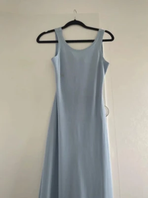 Ljusblå långklänning med öppen rygg - Säljer en stilren ljusblå långklänning i storlek S. Mjukt material. Klänningen har breda axelband, rundad halsringning och en snygg öppen rygg med twistad detalj. Perfekt för dig som vill ha en enkel men ändå unik look. Slits på sidorna.   - har dock en fläck som jag inte fick bort i tvätten. 