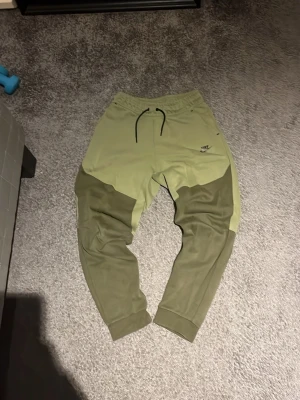 Nike mjukisbyxor i två nyanser grön XL - Snygga mjukisbyxor från Nike i två olika gröna nyanser. Byxorna har snörning i midjan och ribbade muddar vid bensluten. Perfekta för chill eller träning och har en modern, loose passform. Nike-logga på vänster lår.