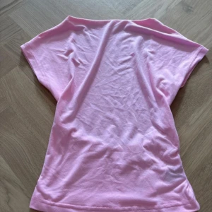 Ljusrosa topp med öppen rygg från SHEIN - Säljer en ljusrosa topp från SHEIN i storlek XS. Toppen har korta ärmar och en snygg öppen rygg med resårdetalj nedtill. Materialet är mjukt och stretchigt polyester, perfekt för dig som gillar en enkel men ändå cool look.