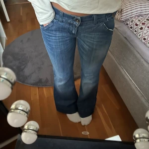 Blå bootcut jeans med låg midja - Snygga blå jeans med bootcut och låg midja. Jeansen har klassisk femficksdesign, slitningar framtill och coola detaljer med knappar på bakfickorna. Köpta för 599kr därav priset❤️