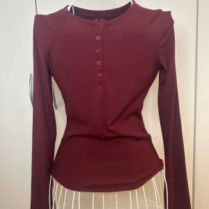 Vinröd ribbad tröja med knappar - Köptes secondhand! Perfekt tröja för layering med ett linne under som sticker ut när man öppnar knapparna. Toppen har en tight passform och är gjord i ett mjukt material, alla knappar fungerar 
