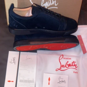 Mörkblå sneakers från Christian Louboutin - Exklusiva mörkblå sneakers från Christian Louboutin i mocka med ikonisk röd sula. Skorna har snörning, rund tå och broderad logga på hälen. Snygg och stilren design som sticker ut med den klassiska röda undersidan.