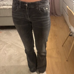 Svarta bootcut jeans från Gina Tricot - Snygga svarta jeans från Gina Tricot i storlek 164. Modellen har bootcut-ben, låg midja och klassiska fem fickor med kontrastsömmar. Jeansen är tillverkade i jeansmaterial och har silverfärgade knappar och detaljer.