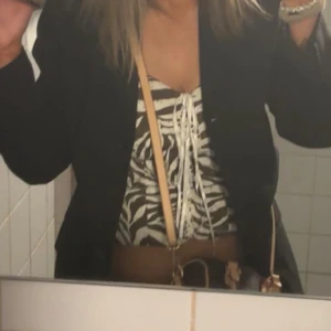 Zebramönstrad snörad linnetopp - Säljer en snygg croppad linnetopp med zebramönster i svart och vitt. Toppen har snörning framtill som ger en cool detalj och v-ringad hals. Perfekt att styla med jeans eller kjol för en trendig look. Den har dragkedja där bak vid ryggen toppen är även stretchig 