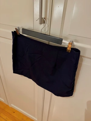 Mörkblå korsymkjol med dragkedja - Enkel och stilren mörkblå kortkjol med rak passform. Kjolen har en diskret dragkedja i sidan. Aldrig använd 