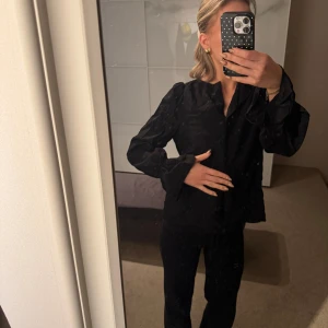 Svart skjorta med vida ärmar - Stilren svart skjorta med långa, vida ärmar och klassisk krage. Skjortan har knappar framtill och en något lös i passformen som ger en avslappnad men ändå dressad look. Perfekt för dig som gillar minimalistisk stil.🩷
