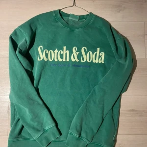 Scotch & Soda Sweatshirt - Snygg grön sweatshirt från Scotch & Soda med stor logotyp i vitt på bröstet och texten 'Free Spirit of Amsterdam' i lila. Tröjan har rund hals, långa ärmar och ribbade muddar. 