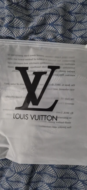 Grå rutig mössa med L v-logga - Grå mössa från L v med diskret rutmönster och uppvikt kant. Framtill sitter en vit patch med svart L v-logga. Mössan är stickad och har en exklusiv känsla, perfekt för dig som vill ha en clean och lyxig look.