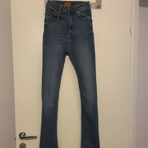 Blå bootcut jeans från O Denim - Snygga blå jeans från O Denim med bootcut passform och hög midja. Jeansen har klassiska fem fickor, slitdetaljer och slits vid benslutet. Materialet är stretchigt. Liten i storlek. 
