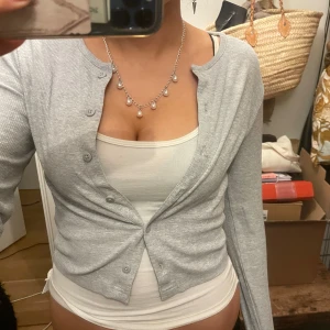 Ljusgrå ribbad kofta med knappar - Säljer en ljusgrå ribbad kofta med rund hals och knappar framtill. Koftan har lång ärm och sitter snyggt och figurnära. Perfekt att slänga över ett linne eller t-shirt för en chill look.