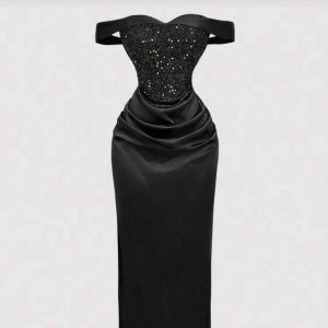 Ball/brölopps klänning, Svart glittrig långklänning - Supersnygg svart långklänning med glittrig överdel och offshoulder-band. Klänningen har figurnära passform, draperad midja och en elegant, slät kjol i satinliknande material. Perfekt för dig som vill sticka ut med en glamorös look.