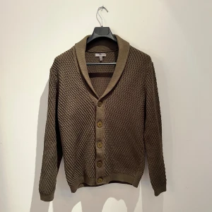 Militärgrön stickad kofta från ASOS - Säljer en militärgrön stickad kofta från ASOS med snygg struktur och bred krage. Koftan har långa ärmar och stängs med snygga knappar framtill. Perfekt för lager-på-lager och chill höststil. Hör av er vid frågor 