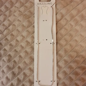 Glittrigt halsband från Dazzling - Ett nytt snyggt halsband från Dazzling i silverfärg med glittrande stenar längs hela kedjan. Nickelfritt. 