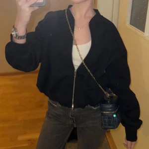 Svart bomberjacka med dragkedja - Svart bomberjacka med hel dragkedja framtill och avslappnad passform. Jackan har långa ärmar och en klassisk, enkel design som passar till det mesta. Perfekt för dig som gillar en stilren och clean look.