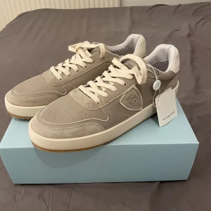 Gråa sneakers från Philippe Model - Säljer ny mina snygga gråa sneakers från Philippe Model. Skorna har ovandel i mocka och skinn, vita snören och diskret logga på sidan. Platt sula i vitt och gummi. Nypriset är ca 3200. Skorna är helt nya och har storlek 44. Priset är inte hugget i sten och om det finns några frågor är det bara att skriva!/Erik