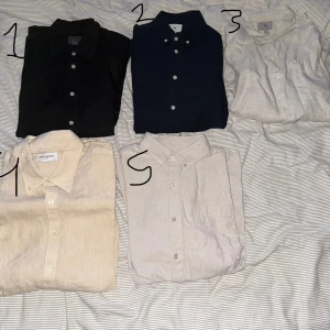 Fem skjortor  - 1. Svart hm linenblend skjorta storlek xs.  2. Marinblåa hm Oxford skjorta storlek xs  3. Beige hm linneskjorta storlek S  4. Beige John Henric linneskjorta storlek 44 5. Beige scw Oxford skjorta storlek S