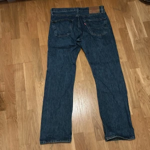 Levi's 501 jeans mörkblå W30 L30 - Klassiska Levi's 501 jeans i mörkblå tvätt med raka ben och knappgylf. Snyggt retro-vibe med fem fickor och ikonisk läderpatch bak i midjan. Perfekt för dig som gillar tidlös stil och äkta denim.