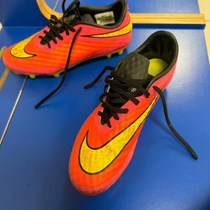 Nike Hypervenom fotbollsskor orange/gul - Säljer ett par Nike Hypervenom fotbollsskor i en riktigt fin orange färg med stora gula swoosh-loggor. Skorna har svart snörning, låg profil och mönstrad ovandel i syntetmaterial. Perfekta för dig som vill sticka ut på planen!