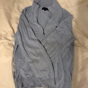 Ljusblå Lexington half zip tröja - Snygg ljusblå tröja från Lexington med half zip och hög krage. Tröjan är stickad i mjuk bomull och har långa ärmar samt ribbade muddar vid ärmslut och nederkant. Perfekt för lager-på-lager och chill stil.