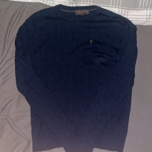 Marinblå kabelstickad tröja Morris - Säljer en marinblå kabelstickad tröja från Morris i 100% merinoull. Tröjan har rund halsringning, diskret broderad logga på bröstet och ribbade muddar. Perfekt för dig som gillar klassisk och stilren look.